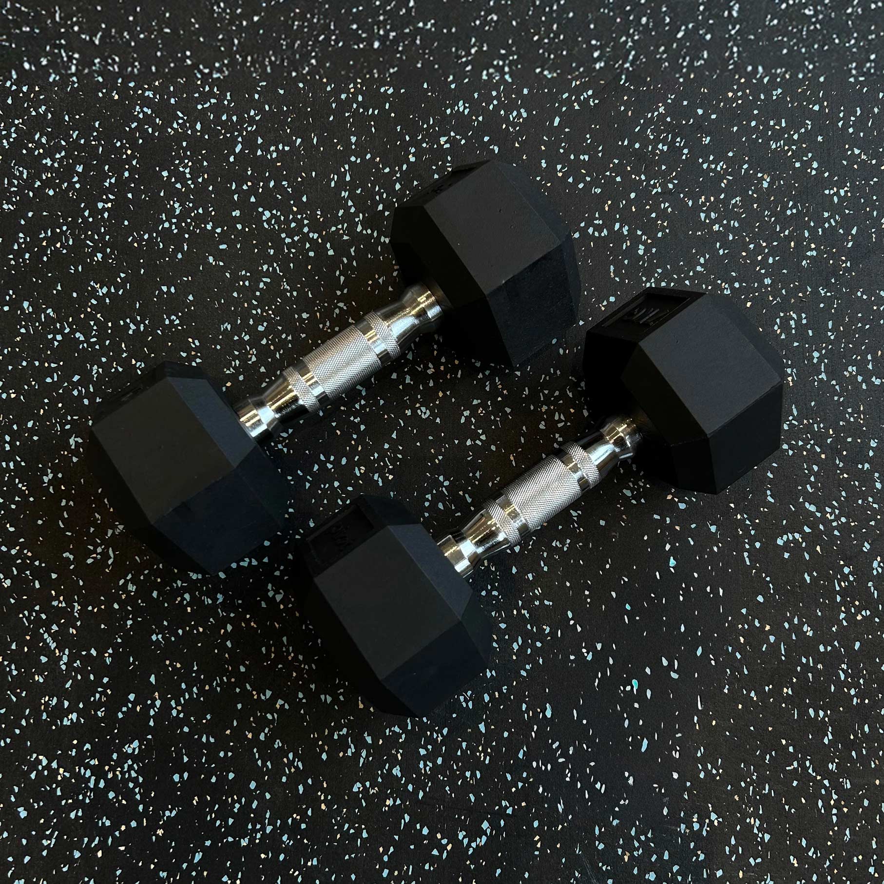 Ett par hexhantlar på ett svart gymgolv med ett ljust mönster