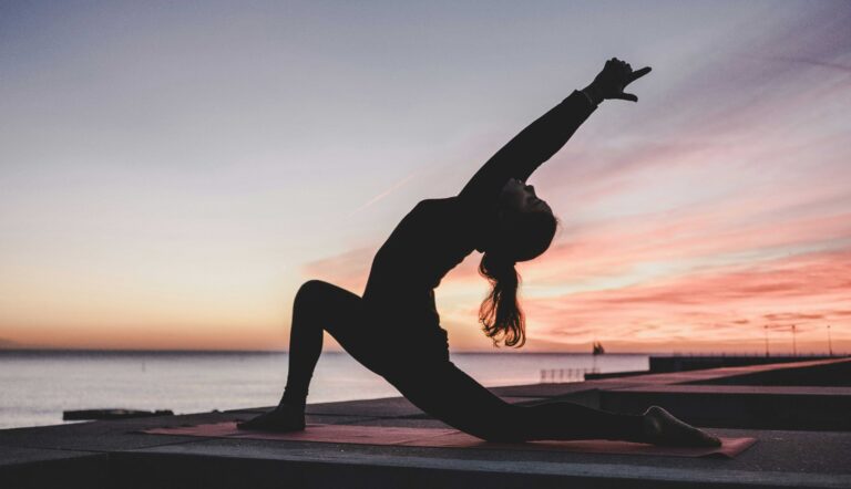 En kvinna som står i yogaposition utomhus vid vattnet