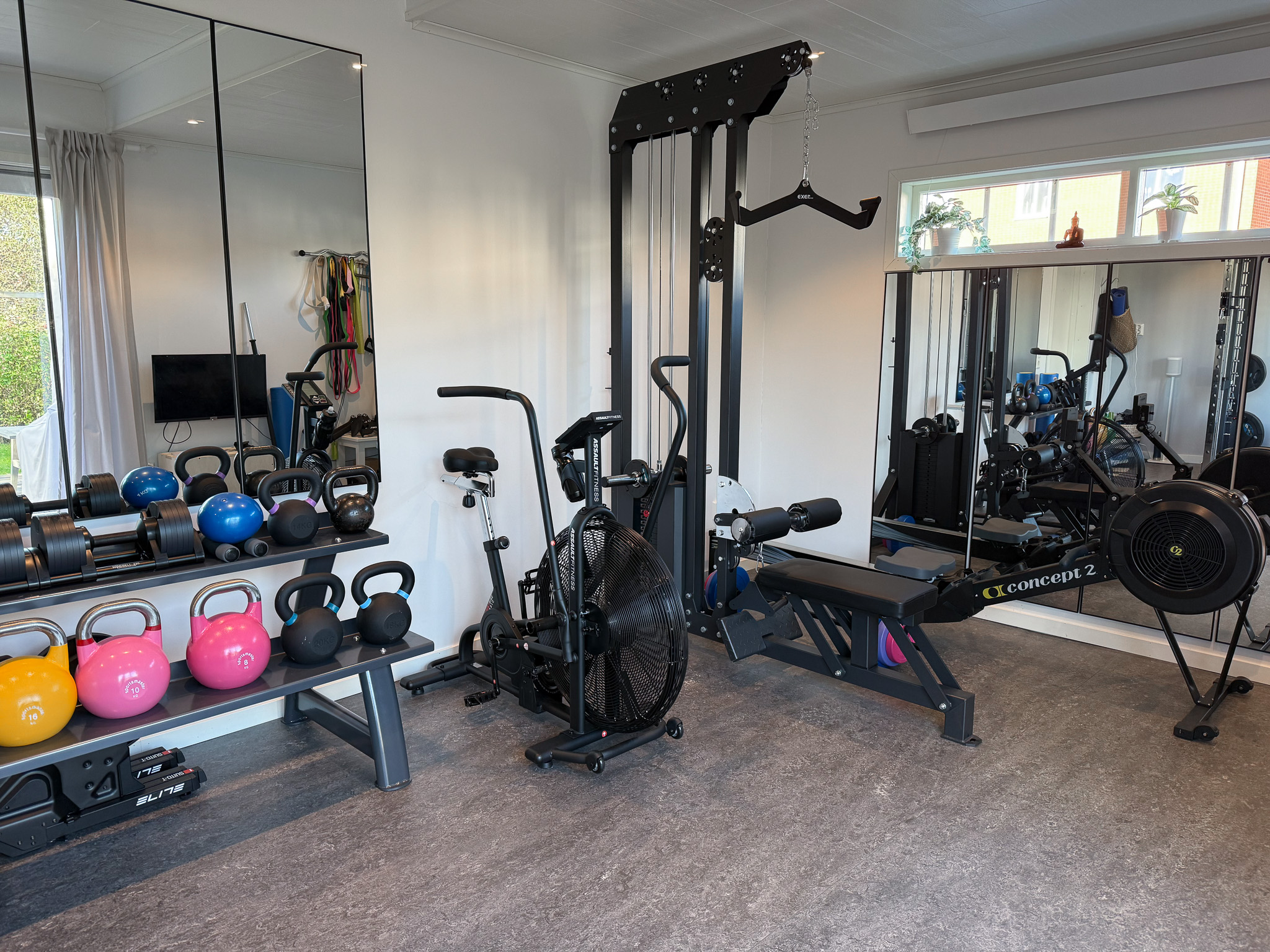 Ett hemmagym med en styrkemaskin, konditionsmaskiner och ett ställ med kettlebells