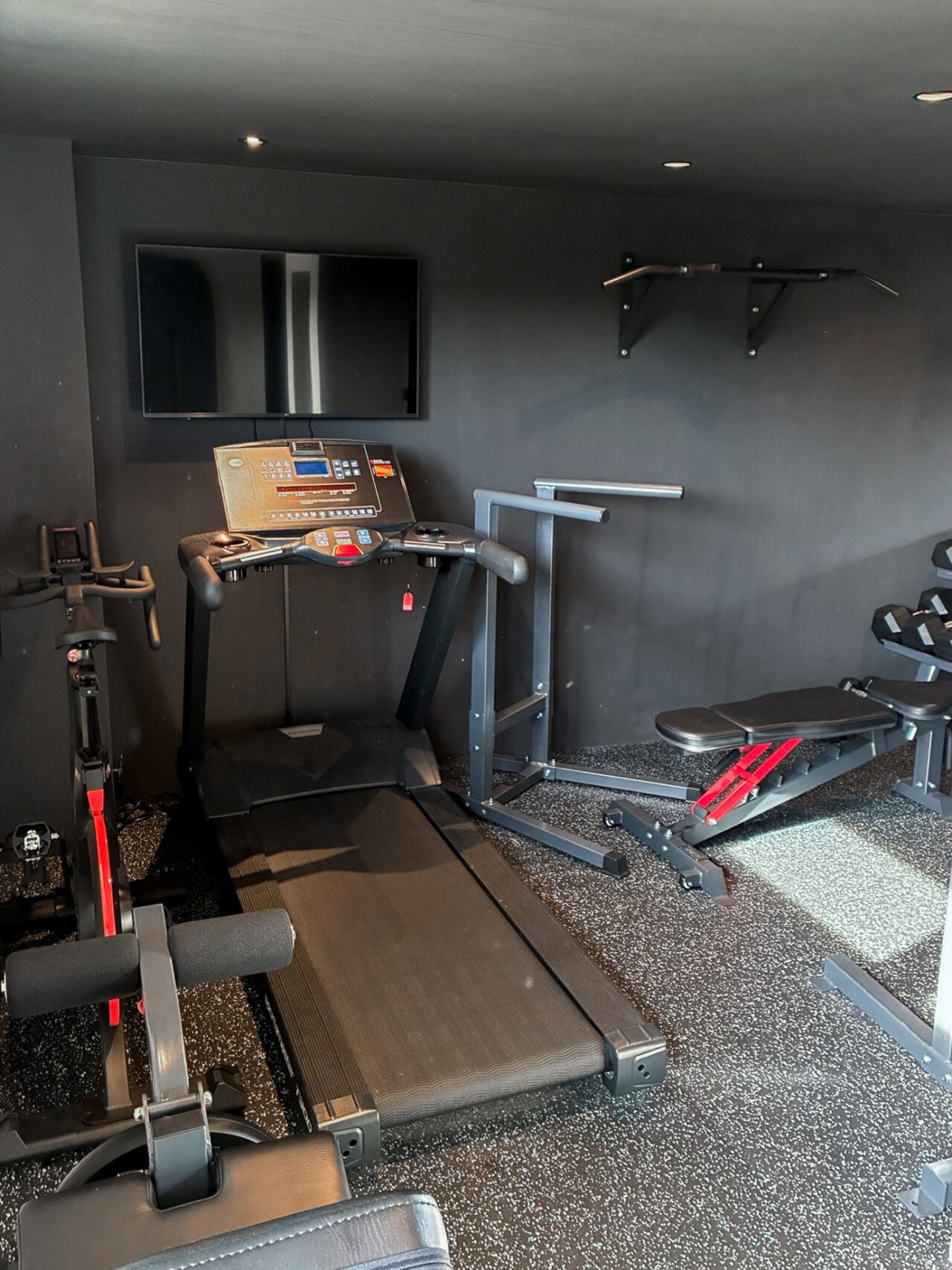 En spinningcykel, ett löpband, ett stativ för dips och en träningsbänk i ett hemmagym