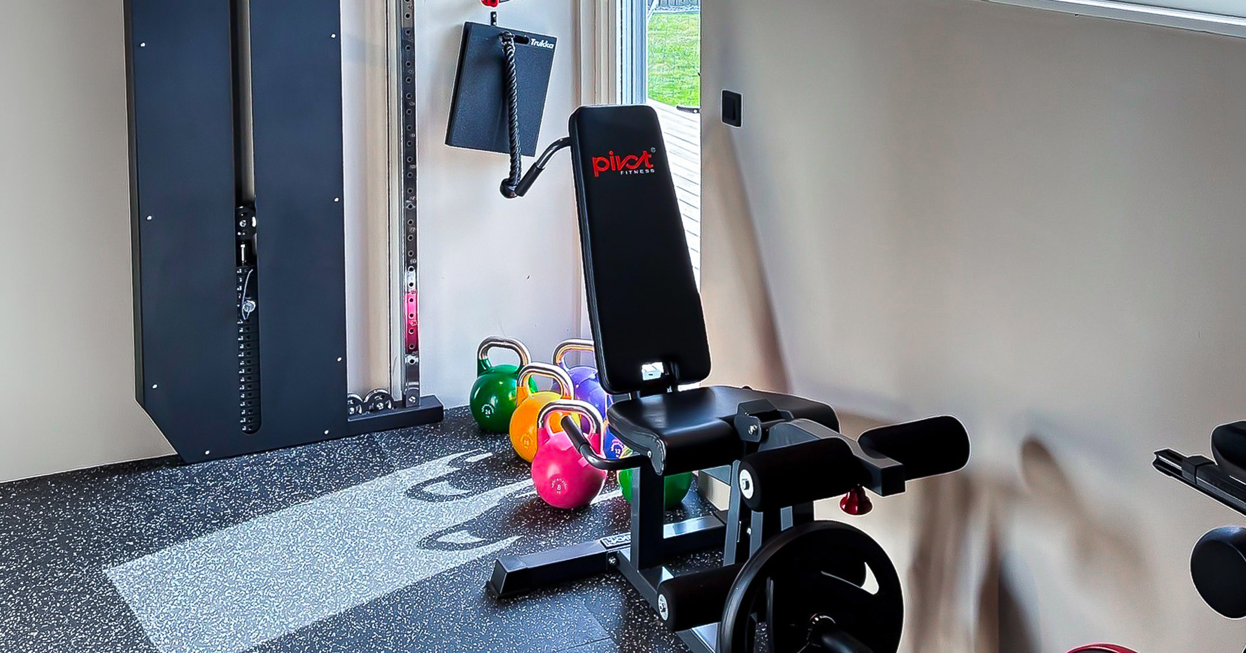 Ett hemmagym med en vägghängd slimmad kabelmaskin, kettlebells och en styrkemaskin