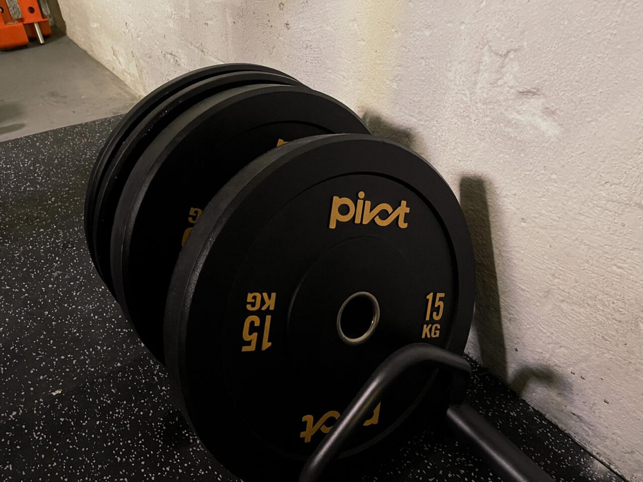 Svarta bumper plates med orange viktmarkering och Pivot logga i ett svart viktställ på golvet